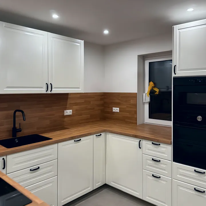 Dieselbe Küche mit schwarzer Spüle und Hochschrank mit Backofen.