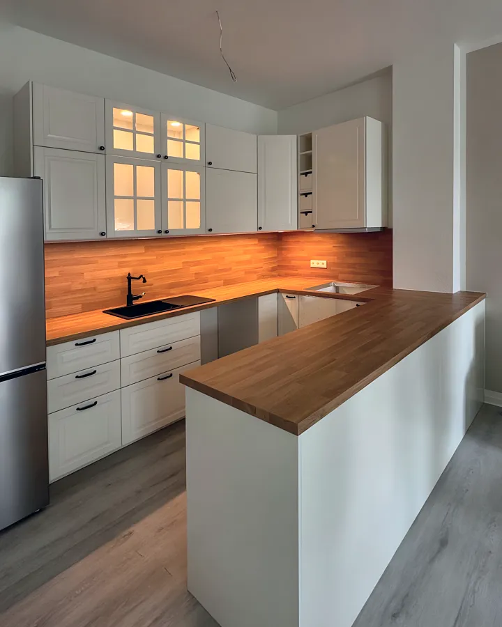 Weiße Küche mit dunkler Holzplatte und beleuchteten Vitrinen.