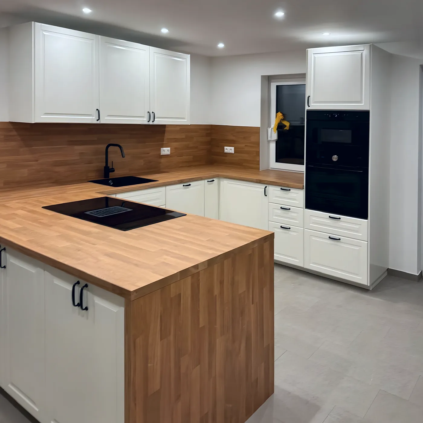 Weiße Küche mit Halbinsel aus Holz und schwarzem Backofen.